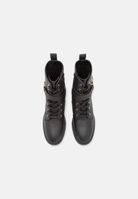 Paire de bottines noires en cuir avec lacets, fermeture éclair latérale et sangle décorative avec boucle dorée, vues de dessus sur fond blanc.