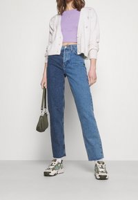 Ljus beige cardigan med blommönster, lila kort topp, tvåtonad blå jeans och flerfärgade sneakers. Olivgrön handväska.