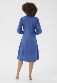 Blauwe jurk tot de knie met pofmouwen, met een getailleerde taille en een zachte textuur. Het ontwerp bevat subtiele plooien en een klassieke kraag.