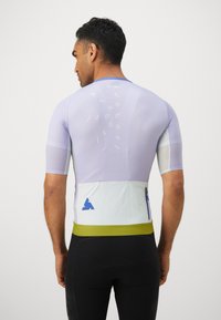 Maillot de cyclisme à manches courtes en lavande clair avec un tissu en maille, une poche blanche, un logo bleu et une ceinture verte, avec un détail textuel au dos.