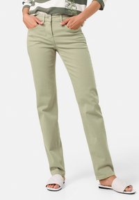 Hellgrüne Hose im geraden Schnitt mit Fronttaschen und Knopfverschluss. Kombiniert mit weißen Stepp-Sandalen.