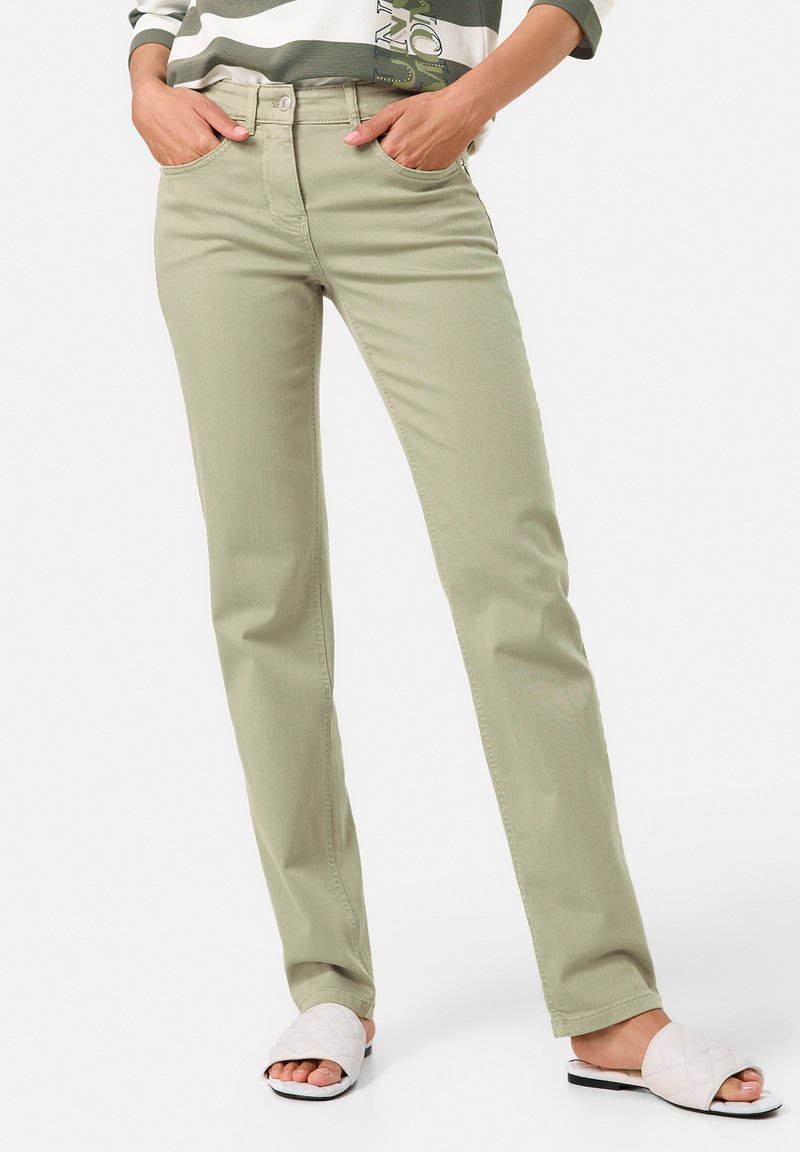 Hellgrüne Hose im geraden Schnitt mit Fronttaschen und Knopfverschluss. Kombiniert mit weißen Stepp-Sandalen.