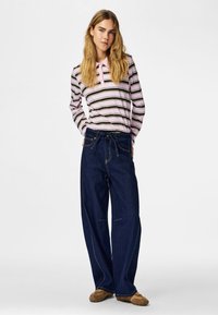 Camiseta de manga larga a rayas en rosa y verde oscuro, combinada con vaqueros de pierna ancha azul oscuro. El conjunto incluye una cintura con cordón y costuras en contraste.