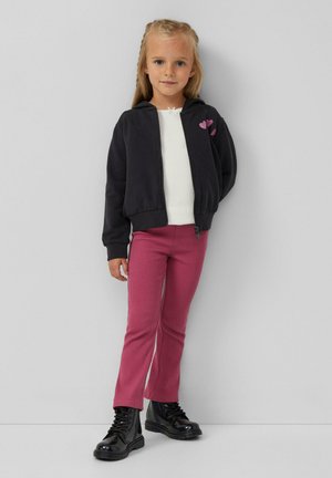 Zwarte zip-up hoodie met roze hart borduurwerk, witte lange mouwen top, roze ribbroek en glanzende zwarte enkellaarsjes.