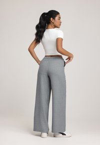 Grijs gestreepte wijde broek met een relaxte fit, voorzien van een trekkoord in de taille en zijzakken. Gecombineerd met een aansluitende witte crop top.