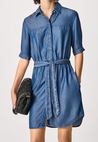 Denim dress featuring short rolled sleeves, a collar, a waist tie, and a button-down front. The fabric has a smooth, soft texture.