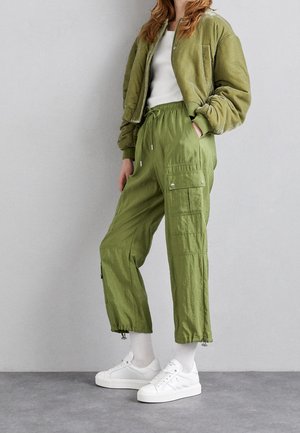 Veste bomber cropped vert clair avec un pantalon à cordon de serrage, doté de poches cargo, associé à des baskets blanches et des chaussettes à mi-mollet.