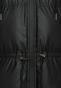 Giubbotto imbottito nero con zip frontale, vita regolabile con cordino e texture liscia e lucida. Due tasche frontali con dettagli in metallo.