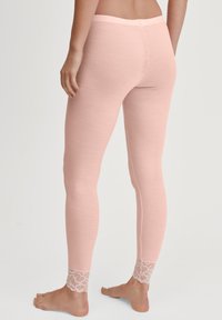 Persoon in lichtroze geribbelde leggings met kantafwerking bij de enkels, staande op blote voeten tegen een witte achtergrond.