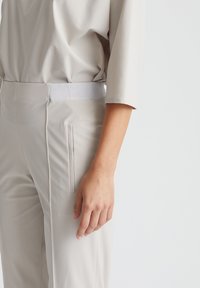 Lichtbeige hoge taille broek van gladde stof, met een platte tailleband en zijzakken in een strakke uitvoering.