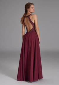 Robe de soirée bordeaux avec un corsage ajusté agrémenté de perles, un design dos nu, et une jupe fluide de longueur maximale.