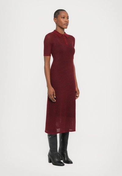 Red and navy striped midi dress with short sleeves, polo collar, and a relaxed fit. Worn with tall black leather boots.