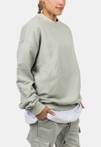 Lysegrøn, oversized sweatshirt lavet af blødt stof, med rund hals og ribbede manchetter, lagdelt over en hvid skjorte.