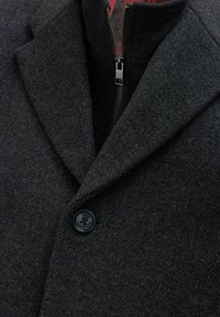 Abrigo de mezcla de lana gris oscuro que presenta un cuello con solapa, un cierre frontal de cremallera y un botón negro redondo en el cuello. Tela texturizada.