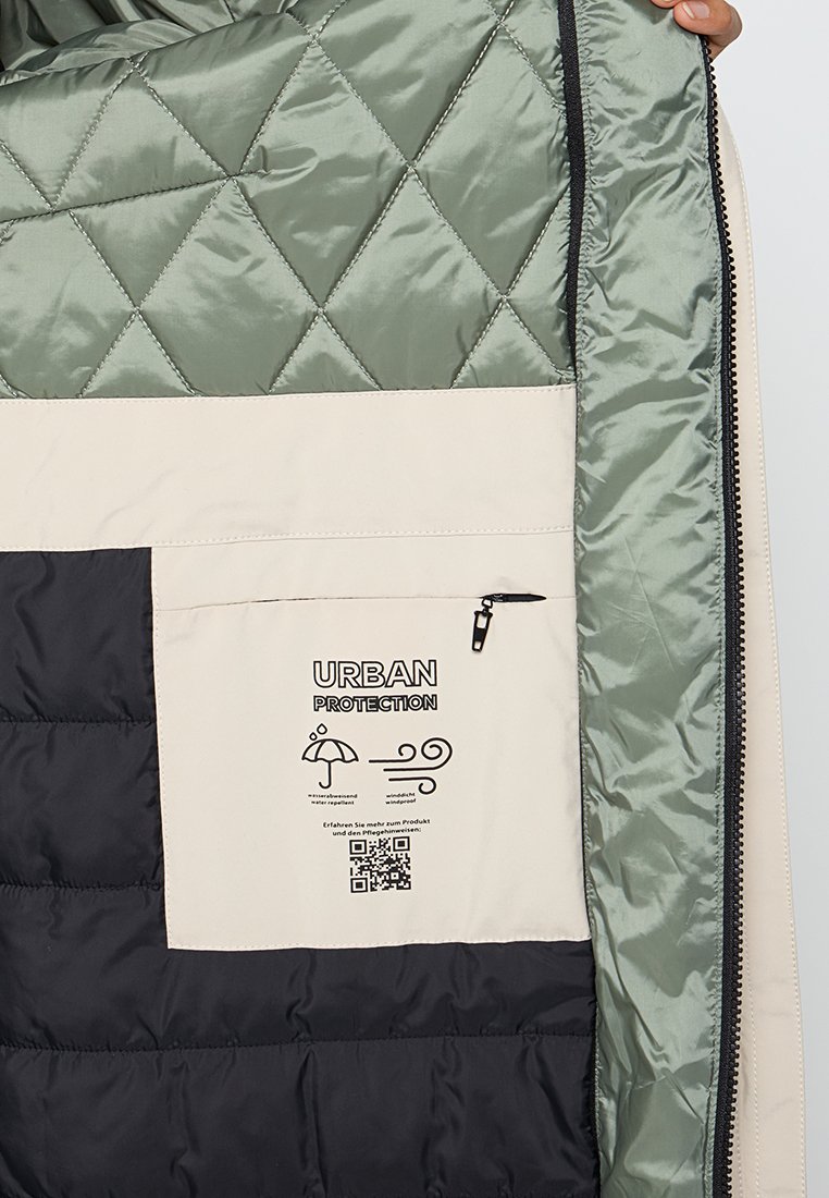 Intérieur de veste matelassée en vert et noir avec une poche beige étiquetée "Urban Protection", fermeture éclair, icônes météorologiques et code QR.