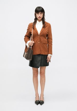 Barna velúrblézer, fehér blúz, fekete bőr szoknya és hegyes orrú fekete magassarkú. Barna táska mintás díszítéssel. Bojtokkal díszített táskafüggő.