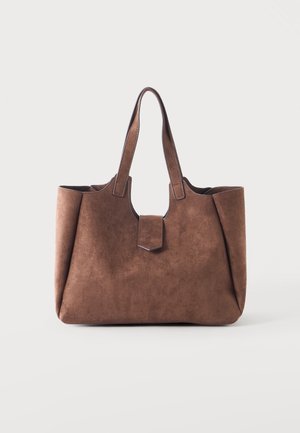 Sac cabas en daim marron avec deux poignées et une petite fermeture à rabat avant sur un fond clair uni.