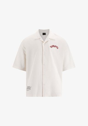 Camisa de manga corta y botones en tejido color blanco roto, con texto bordado en rojo en el pecho y detalle del logo en negro en el dobladillo.