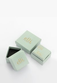 Trois boîtes à bijoux carrées vert clair, deux fermées, une ouverte révélant un intérieur noir, avec des logos dorés « elli premium » sur fond blanc.