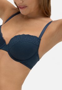 Sujeción azul marino acolchado con encaje en los bordes, tirantes ajustables y una textura suave acanalada, diseñado para ofrecer soporte y comodidad.