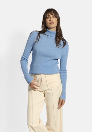 Lichtblauwe geribde coltrui met lange mouwen, gecombineerd met crèmekleurige wijde broek met voorkruiszakken en subtiele verticale naden.