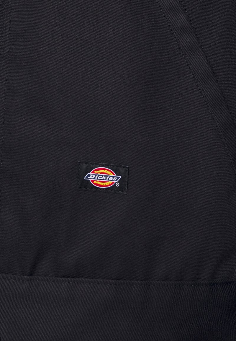 Tela negra con una textura suave que presenta una etiqueta con el logo de Dickies en rojo, amarillo y azul, cosida sobre el material.