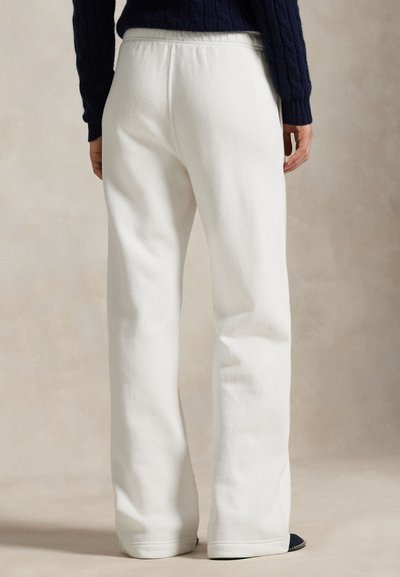 Person iført hvide, løstsiddende sweatpants med højtaljet elastik i livet, kombineret med en mørkeblå kabelstrikket sweater.