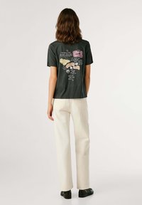 T-shirt grigio scuro con stampa grafica colorata sul retro. Dotato di maniche corte e vestibilità rilassata. Abbinato a pantaloni color avorio e scarpe nere.