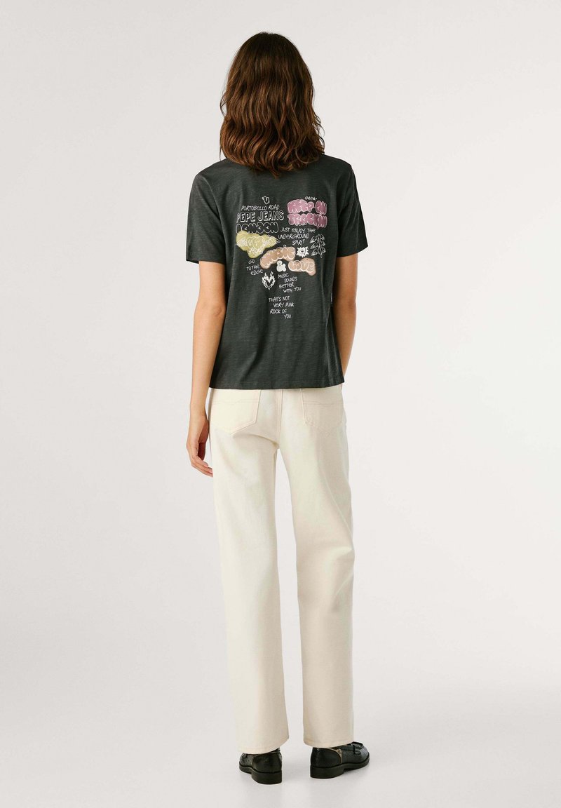T-shirt grigio scuro con stampa grafica colorata sul retro. Dotato di maniche corte e vestibilità rilassata. Abbinato a pantaloni color avorio e scarpe nere.