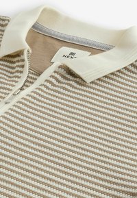 Kurzarm-Polohemd mit einem beigen und weißen Streifenmuster, Reißverschluss und aus einem weichen, strukturierten Baumwollmischgewebe. Mit einem cremefarbenen Kragen.