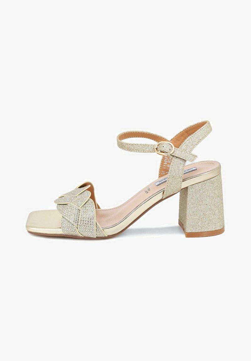 Sandal con tacco quadrato in glitter oro, dotata di dettaglio a fiocco sulla fascia e cinturino alla caviglia regolabile per una vestibilità ottimale.