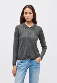 Siv rebrast pulover s ovratnikom, z zapenjanjem na gumbe in subtilnim teksturiranim vzorcem na sprednji strani. Dolgi rokavi in mehki material.