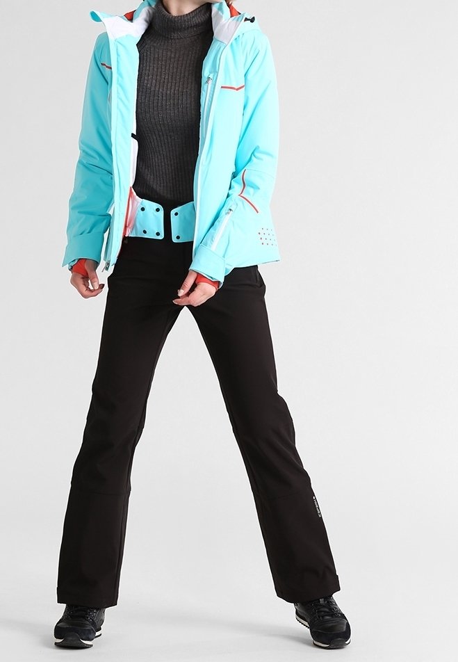 Personne portant une veste d'hiver bleu clair, un pantalon noir, des chaussures noires et un pull à col roulé gris foncé, debout, jambes écartées.