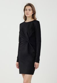 Czarna sukienka z długim rękawem, z przodem ozdobionym skręceniem, o długości do kolan, gładką fakturą materiału i minimalistycznym designie.