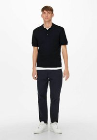 Zwart polo-shirt met korte mouwen, voorzien van een geribbelde kraag. Gecombineerd met marineblauwe broek en witte sneakers, wat zorgt voor een casual uitstraling.