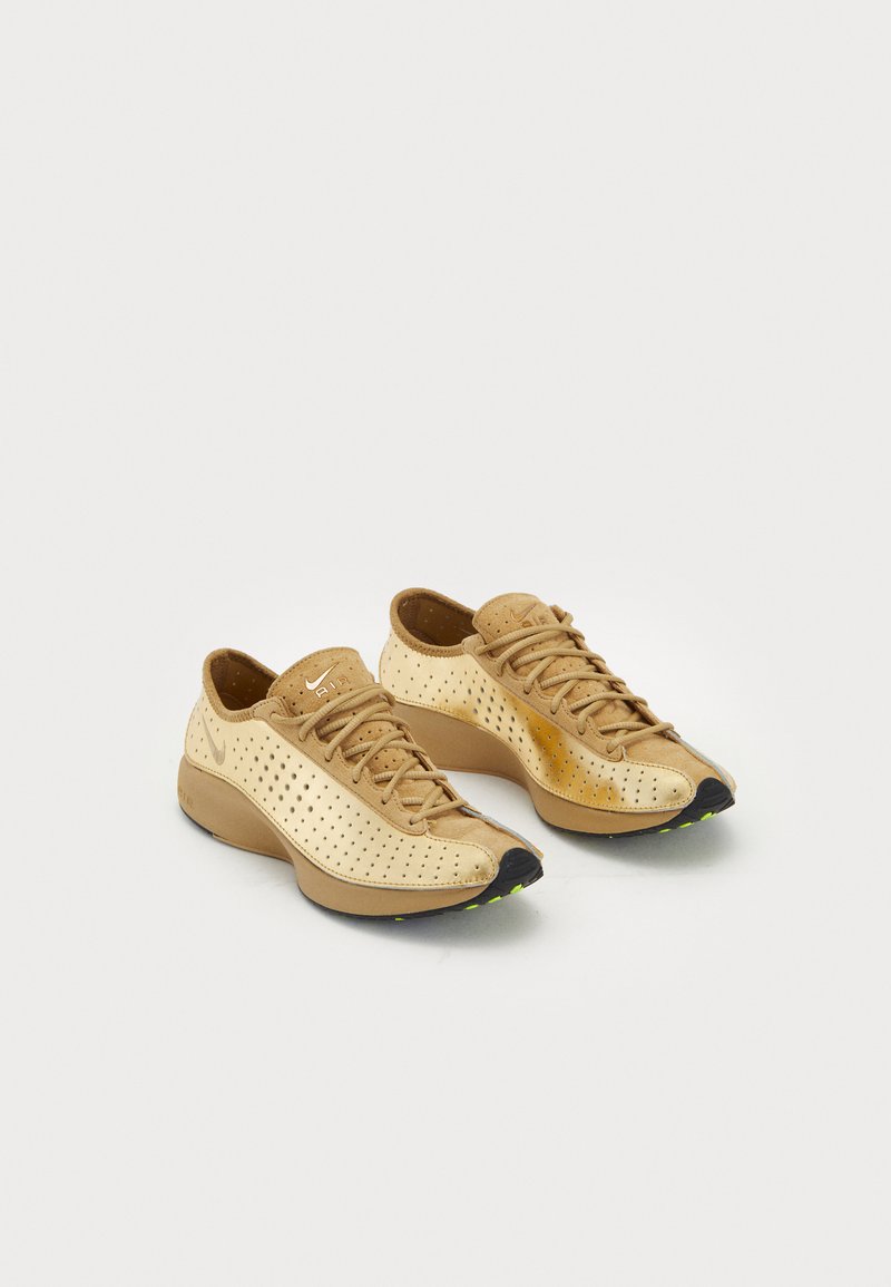 Par tenisica Nike Air u boji bež i smeđe sa perforiranim detaljima, vezicama i crnim potplatima ukrašenim malim zelenim mrljama.