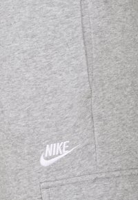 Tissu gris clair avec des coutures visibles et un petit logo Nike brodé en blanc ainsi qu'un swoosh près d'une couture.