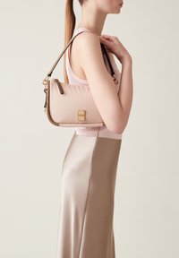 Rosa Nylon-Handtasche mit einer goldenen Schnalle, ausgestattet mit einem geflochtenen Trageriemen und glatter Textur, die an der Schulter vor einem hellen Hintergrund gehalten wird.