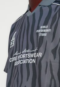 Γκρι αθλητική φανέλα με στο σχέδιο και γιακά σε σχήμα V, με μαύρες ρίγες τίγρης, λευκά λογότυπα κειμένου και υφή υφάσματος με ανάγλυφη όψη.