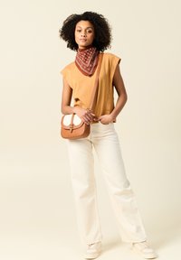 Top senza maniche color tan, bandana rossa a fantasia, pantaloni bianchi a gamba larga e sneakers chiare. Borsa a tracolla con un design marrone e bianco.