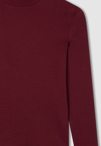 Top lungo a maniche con costine color borgogna e colletto alto. Presenta un tessuto testurizzato e una silhouette aderente. Visibili dettagli delle cuciture lisce.