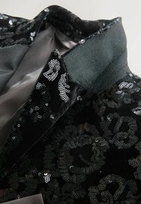 Zwarte fluwelen jasje met een sequin bloemenpatroon, met een satijnen voering en een gestructureerde kraag met een textuurafwerking.