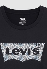 T-shirt en coton noir avec un graphique logo floral Levi's en blanc et bleu. Design classique à col ras du cou, texture lisse et manches courtes.