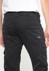 Zwarte cargobroek met een relaxte pasvorm, meerdere zakken en een subtiele versleten detail op de achterzak. Gemaakt van duurzaam materiaal.