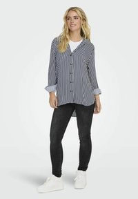 Camisa a rayas en azul marino y blanco, con cuello y puños enrollados, combinada con jeans ajustados negros y zapatillas blancas.