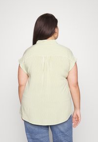 Camisa de manga corta con cuello que presenta rayas verdes claras y blancas. Tejido suave con un corte relajado y detalle de pliegue en la parte posterior.