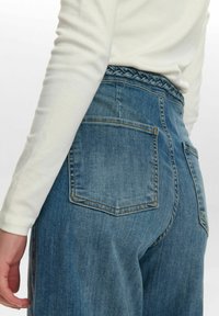 Blå denimjeans med hög midja, elastisk midjeband med dekorativa sömmar och två bakfickor. Tillverkade av bomull med en lätt textur.