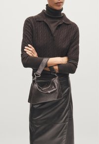 Borsa in pelle nera con una forma curva, chiusura con zip e manico corto, abbinata a un top in maglia marrone testurizzata e a una gonna in pelle nera.