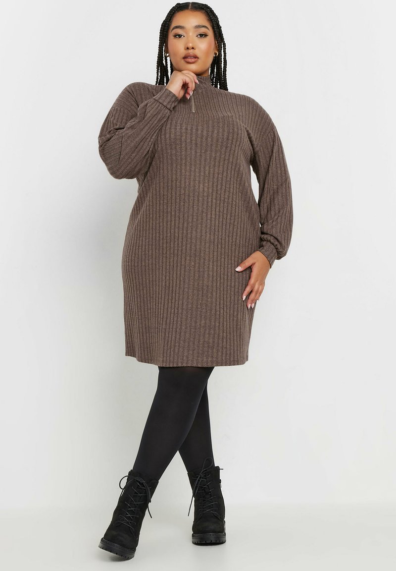 Brun ribbad stickad klänning med hög krage, långa ballongärmar och rak silhuett. Bärs med svarta ogenomskinliga strumpbyxor och ankelstövlar.