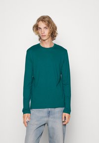 Langærmet skjorte i teal lavet af blødt stof, med rund hals og lige pasform, parret med lyseblå denim jeans.
